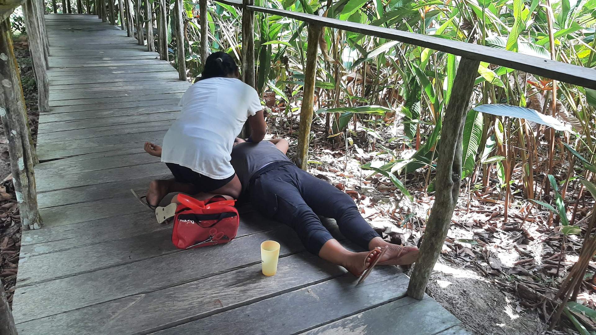 Una participante atiende a una paciente acostada sobre un sendero de madera en la selva, junto a un botiquín